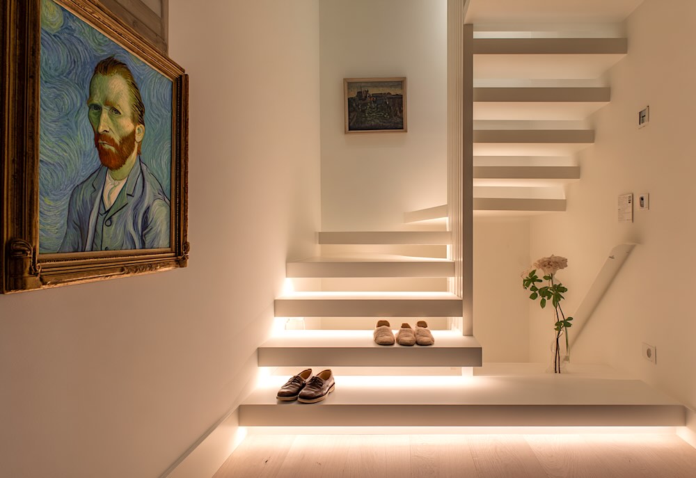 Open trap met ingebouwde sfeervolle LED-verlichting onder elke trede, zwevend effect, luxe moderne woning in Nederland, gezellig en stijlvol, fotorealistische interieurfoto, witte muren, warme verlichting, natuurlijke schaduwen, schilderij van Van Gogh aan de muur, twee paar damesschoenen op de vernieuwde trap, designgericht